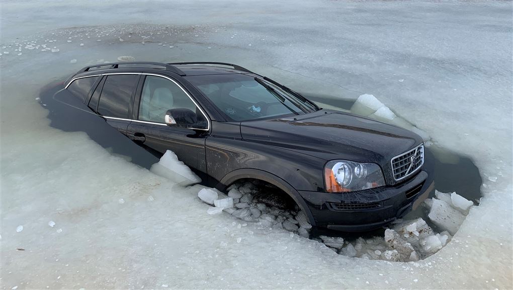 En sort Volvo næsten dækket af vand og omgivet af is. 