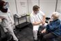 kvinde venter på at få vaccination i lokale med to sundhedspersonaler