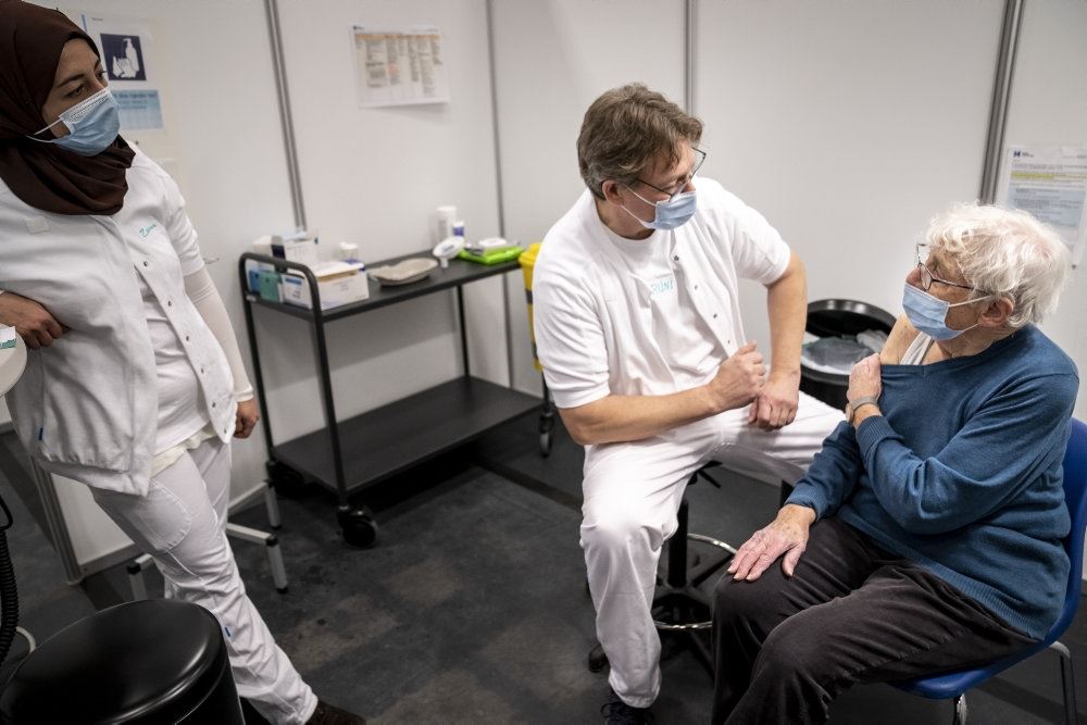 kvinde venter på at få vaccination i lokale med to sundhedspersonaler