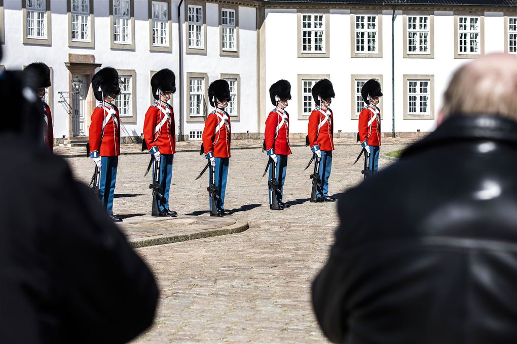 Seks livgardere ses ved Fredensborg slot. De er iført røde uniformer og bjørnehuer. 