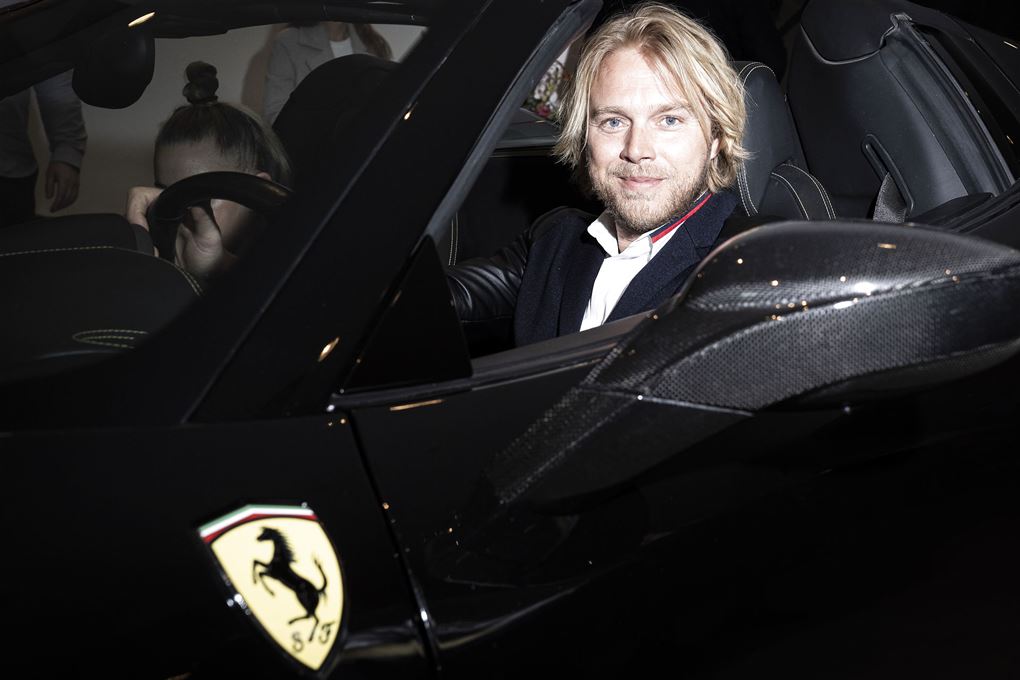 tv-vært Felix Smith sidder bag rattet på en sort Ferrari. 