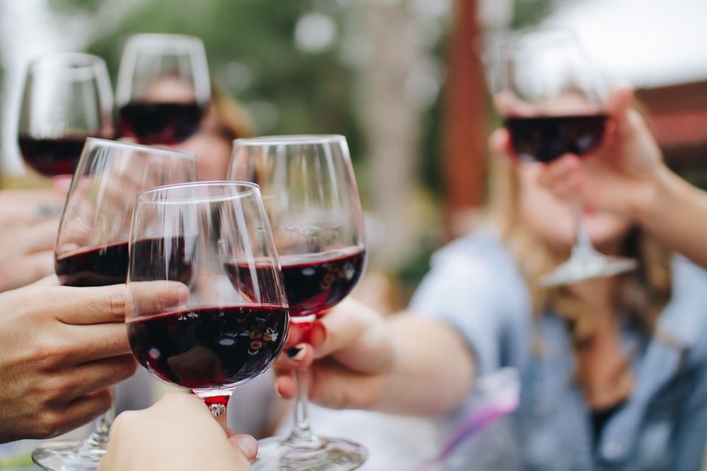 folk sidder udendørs og skåler med rødvin i glassene