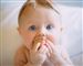 En baby med store blå øjne med en legeklods i munden mens han eller hun kigger direkte ind i kameraet. 