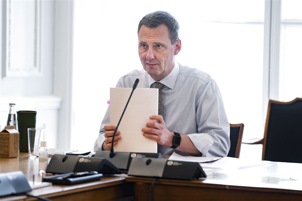 Nick Hækkerup sidder ved et bord med en bordmikrofon foran sig og en stor stak papirer i hånden. 