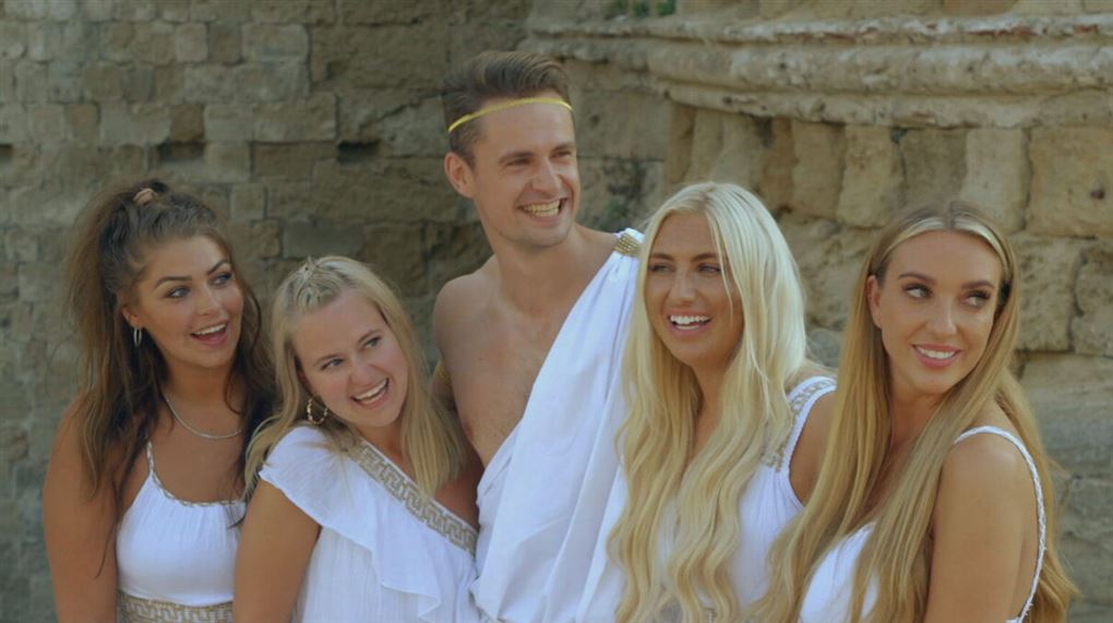 En fyr klædt i lagen flankeret af fire piger i hvide kjoler