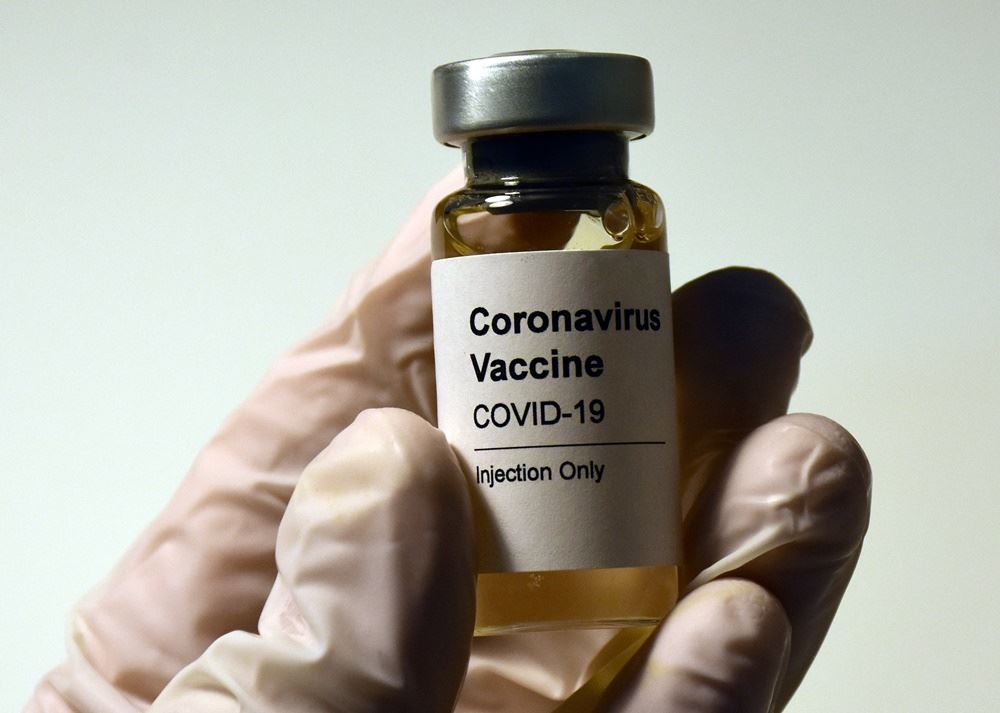 person står med flaske med coronavaccine i hånden