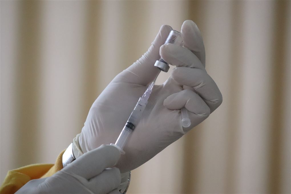 En hånd i latexhandske trækker en vaccinedosis op i en kanyle.