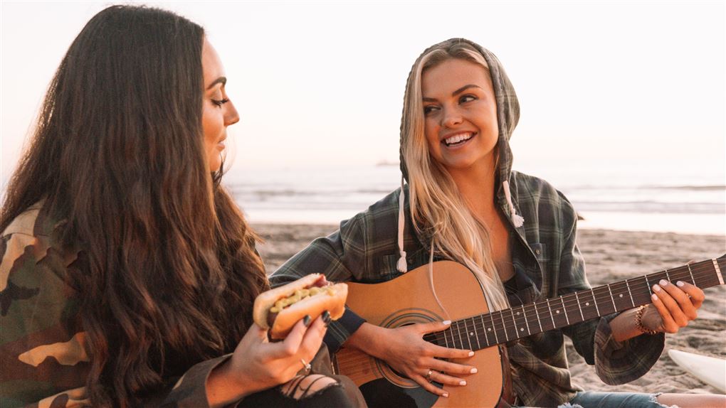 Piger på strand spiller guitar