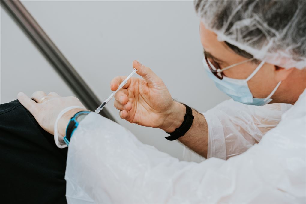 En person fra sundhedsvæsnet iført værnemidler giver en vaccine i en skulder.