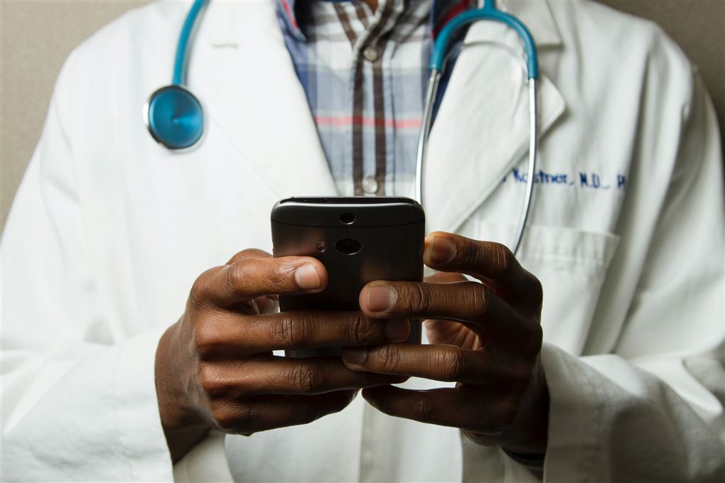 En læge i kittel med en telefon i hånden. 