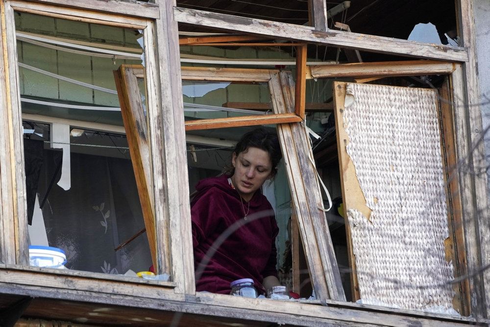 En kvinde kigger ud fra et sønderbombet hus