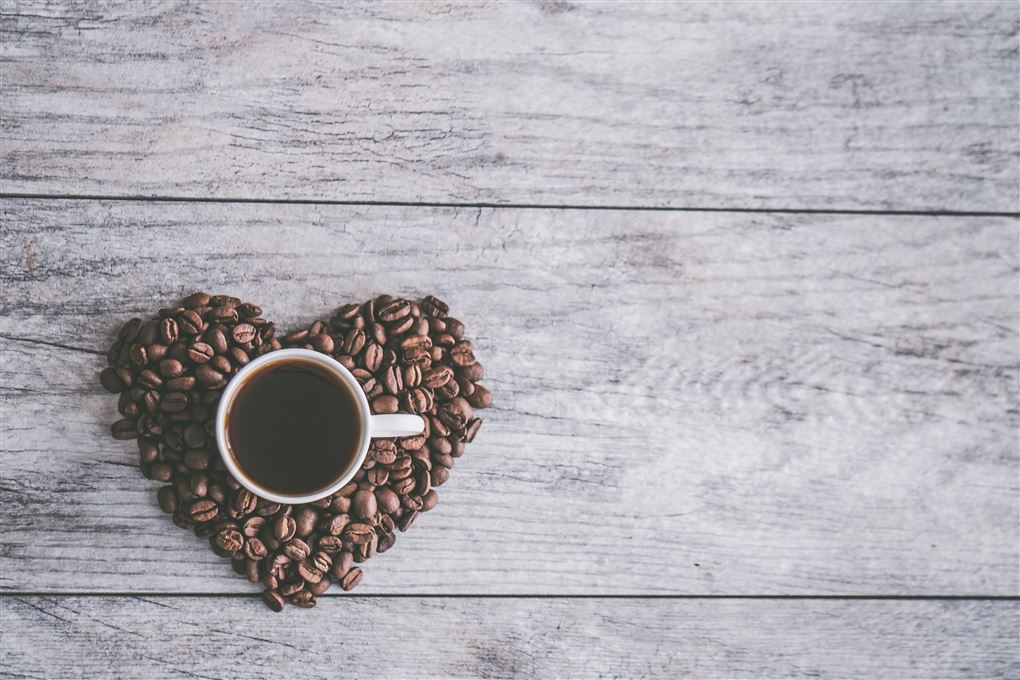 En kop kaffe på nogle kaffebønner formet som et hjerte