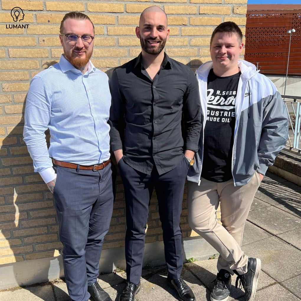 Tre yngre mænd ved en mur
