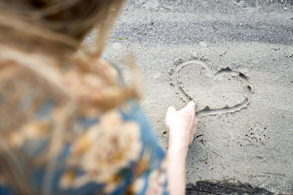 person tegner hjerte i sand