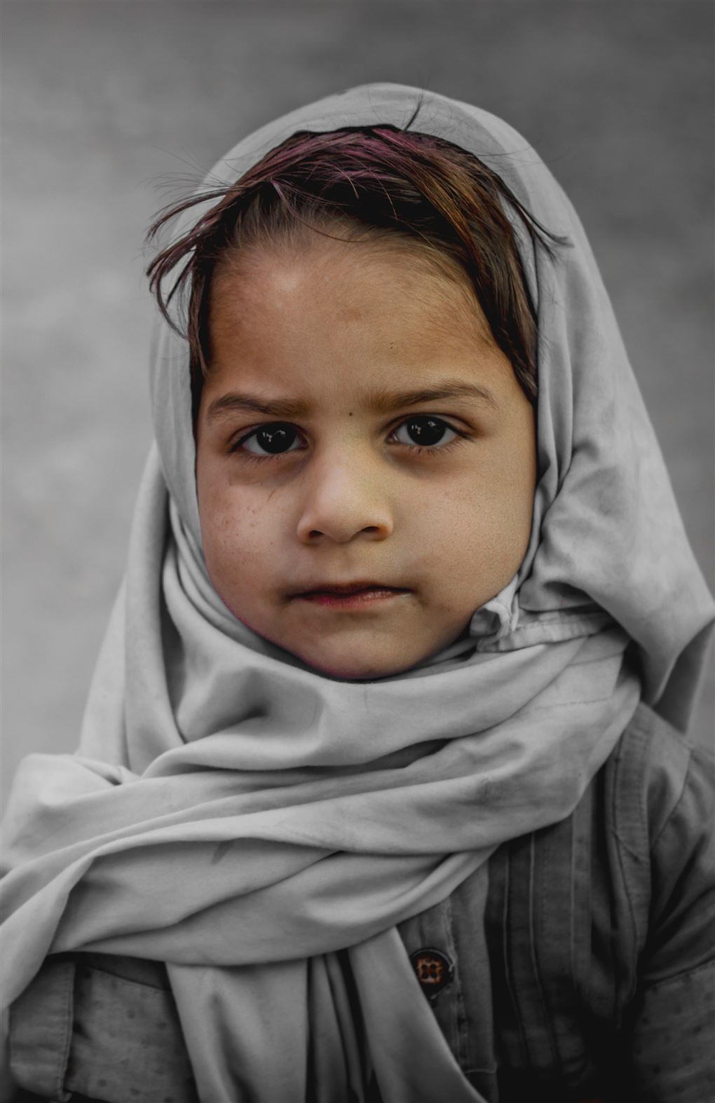 En lille pige med et gråt tørklæde om håret 