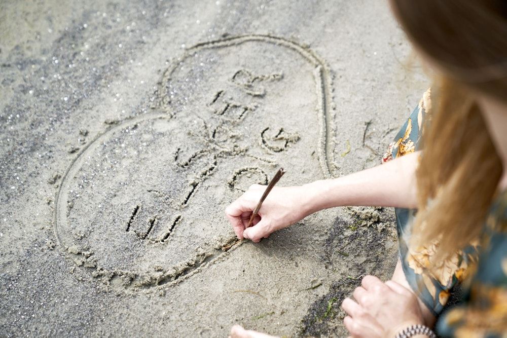 person tegner hjerte i sand