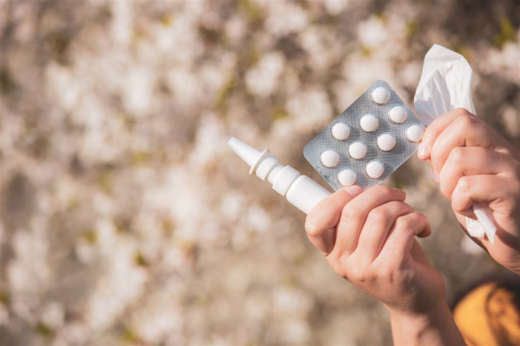 Et sæt hænder holder næsespray, piller og papirservietter. 