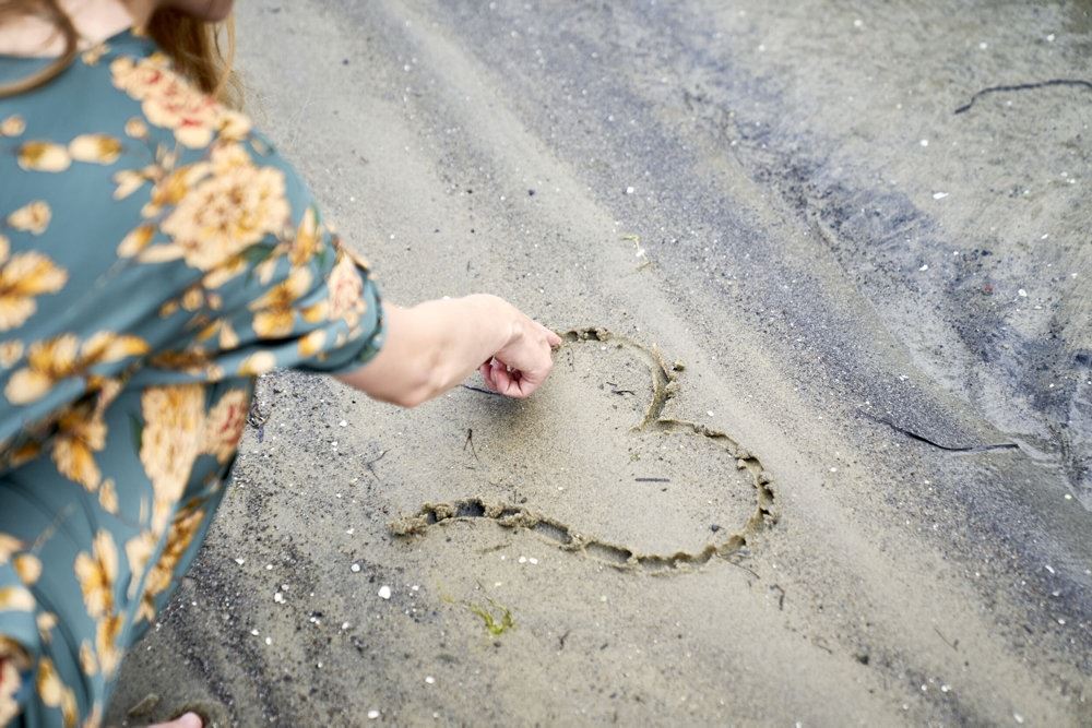 person tegner hjerte i sand