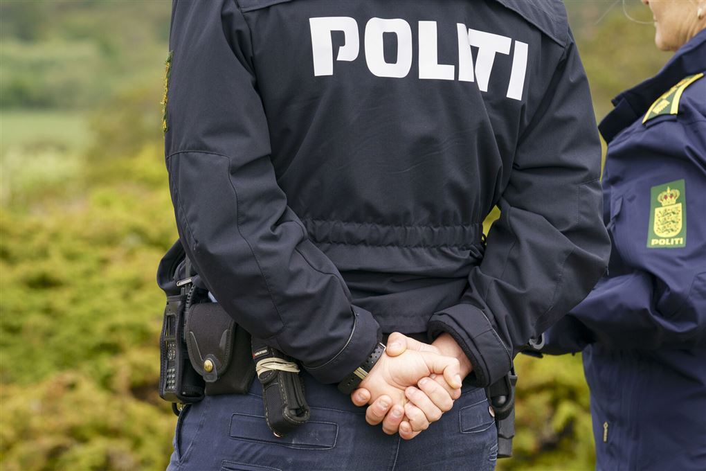 En politibetjent med ryggen til hænderne på ryggen.