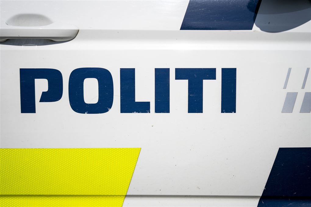 En politibil set fra siden. Den er hvid med blå skrift.