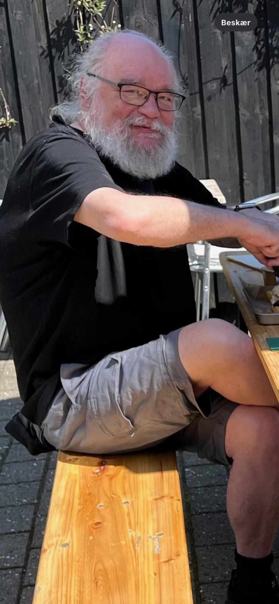 En mand med gråt fuldskæg og briller. Han smiler.