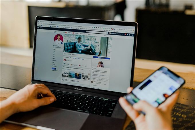 person sidder på facebook på computer og telefon