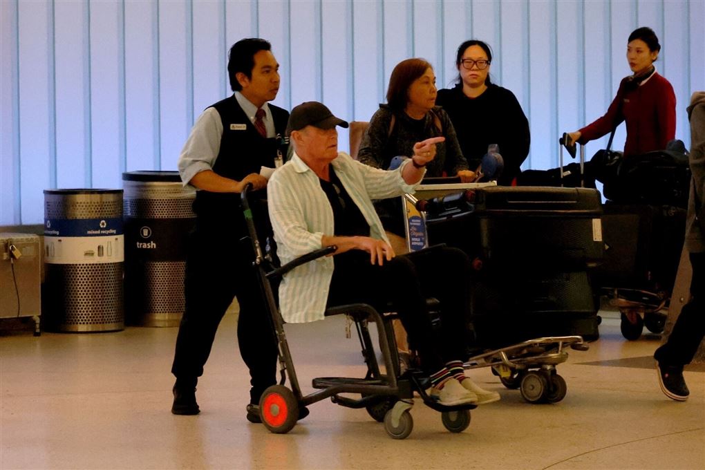 Mand i kørestol med en lufthavnsansat skubbende stolen bag sig. 