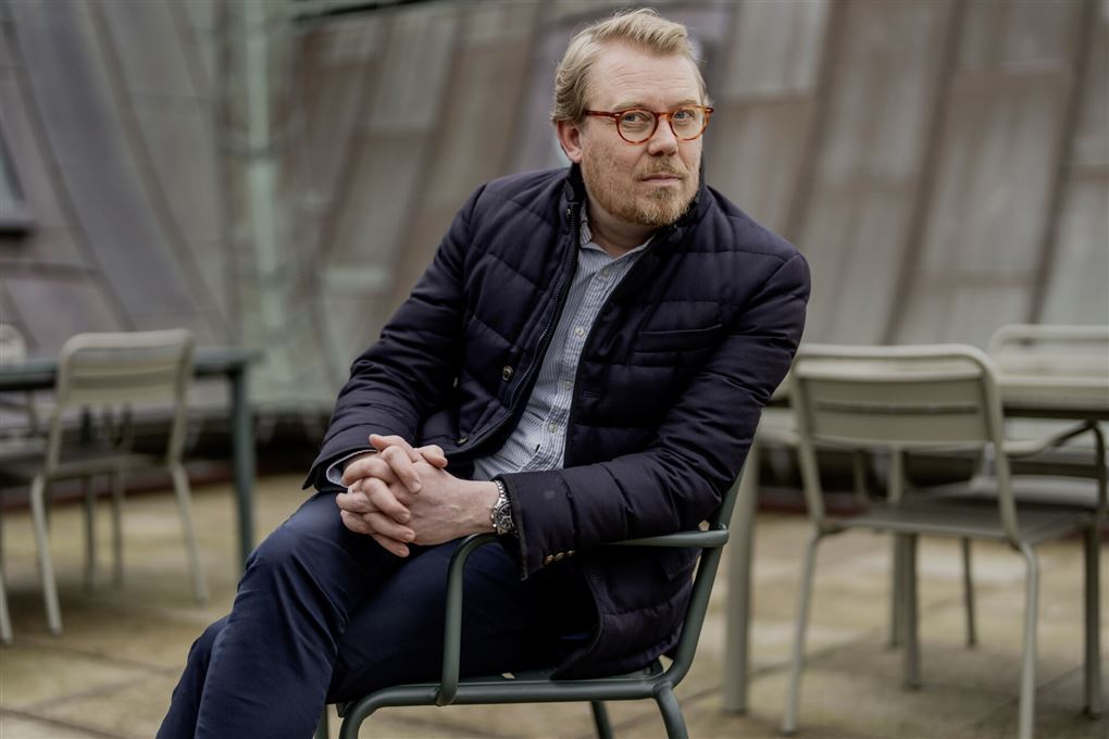 Mand sidder i stol og kigger ind i kameraet.