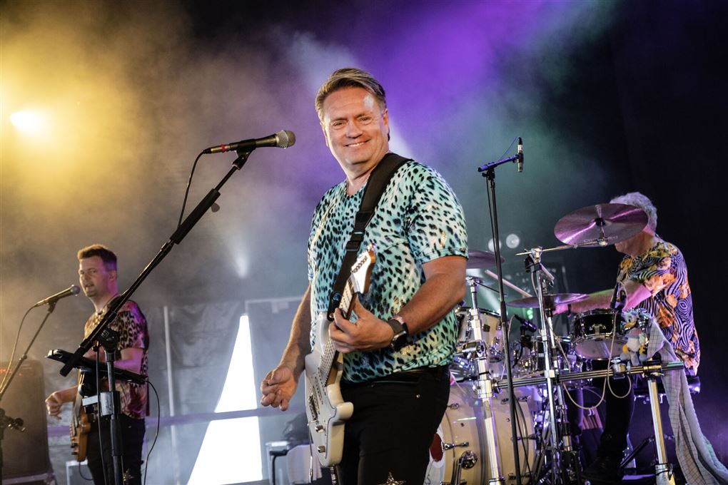 Kandis-Johnny står på en scene med sin guitar og smiler til kameraet