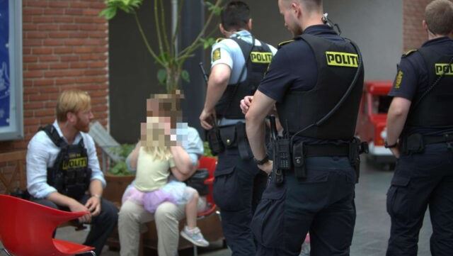 en pige sidder på skødet af sin mor politi står rundt om