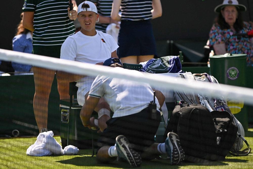 tennisspiller sidder på stol bag nettet