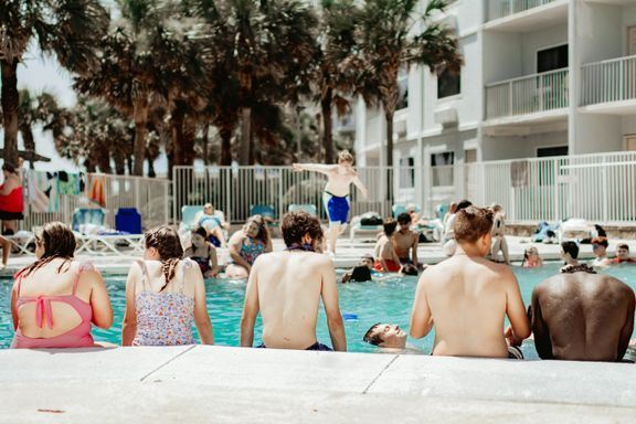 En række mennesker sidder i bar overkrop ved en poolkant